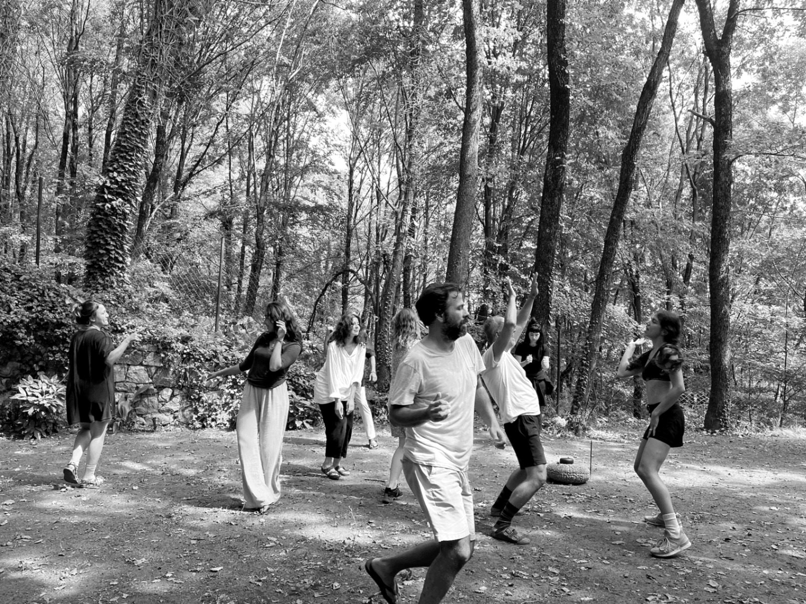 Body as Erotic Site workshop — participants dancing together in a sunlit forest clearing, in black and white